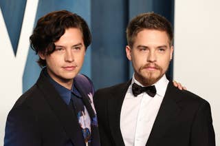 Cole Sprouse and Dylan Sprouse pose together, Cole in a patterned suit and Dylan in a classic black tuxedo, on a formal event red carpet