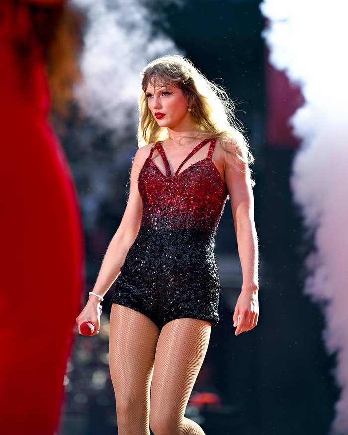 Taylor Swift performing on stage wearing a sparkly red and black romper. Smoke effects in the background