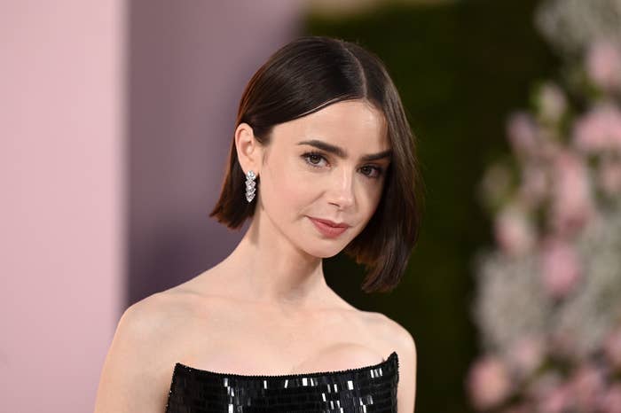 Lily Collins poses at an event wearing a strapless black sequined dress, diamond earrings, and a sleek bob hairstyle